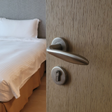 Half open houten deur voorzien van RVS deurklink met een keurig opgemaakt bed op de achtergrond