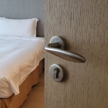 Half open houten deur voorzien van RVS deurklink met een keurig opgemaakt bed op de achtergrond