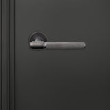 Cosenza PVD gecoate binnendeurkruk Gun Metal met Knurled motief op donkere deur, vooraanzicht