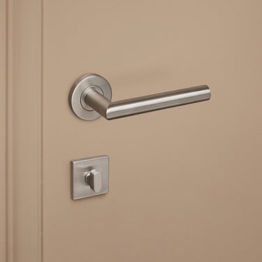 RVS vierkant WC-rozet binnenzijde met draaiknop en RVS deurkruk op beige deur, linkeraanzicht