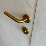 Oristano deurklink met PVD coating in het mat goud. sfeerbeeld op een lichtgekleurde deur