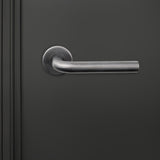 Lavuzo Oristano deurklink Gun Metal PVD op rond rozet strak gemonteerd op donkere binnendeur, vooraanzicht
