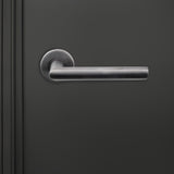 Lavuzo Ragusa deurklink Gun Metal PVD op rond rozet strak gemonteerd op donkere binnendeur, vooraanzicht